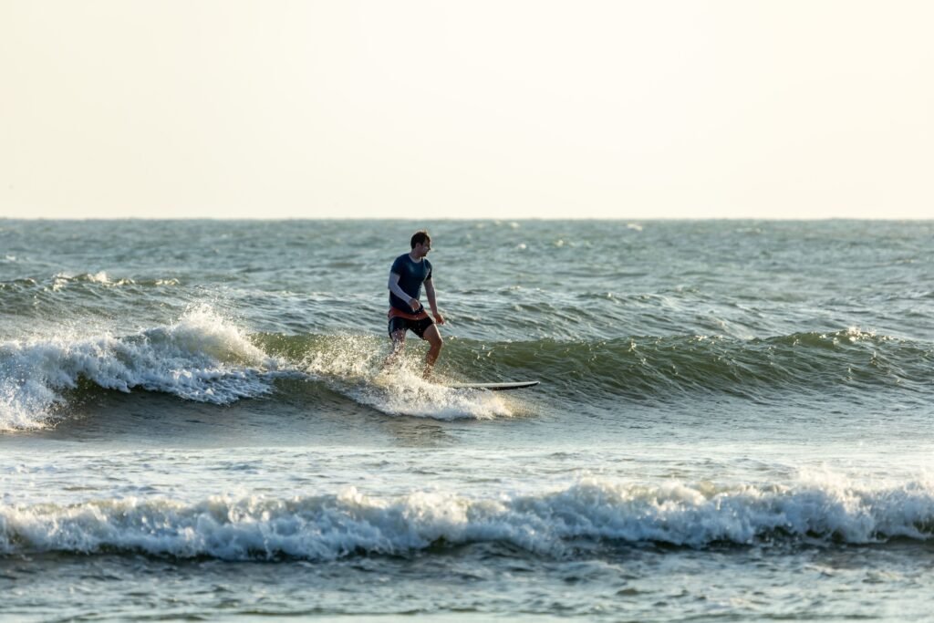 A lone surfer skillfully navigates gentle waves under a warm sunset sky.