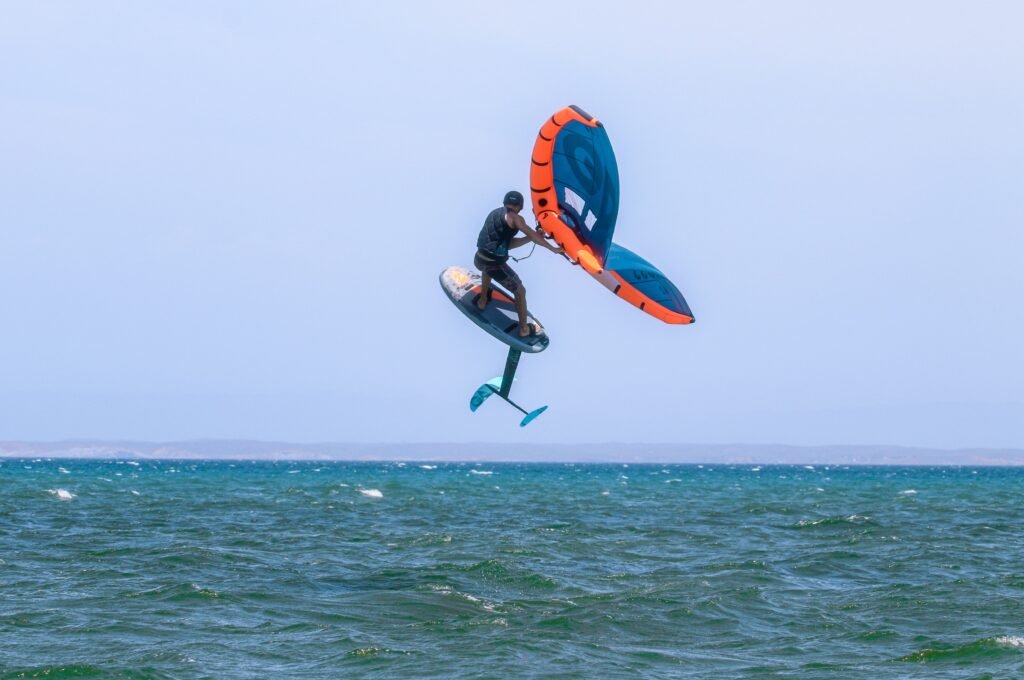 A kitesurfer executes a high jump above ocean waves, showcasing skill and adventure on a sunny day.