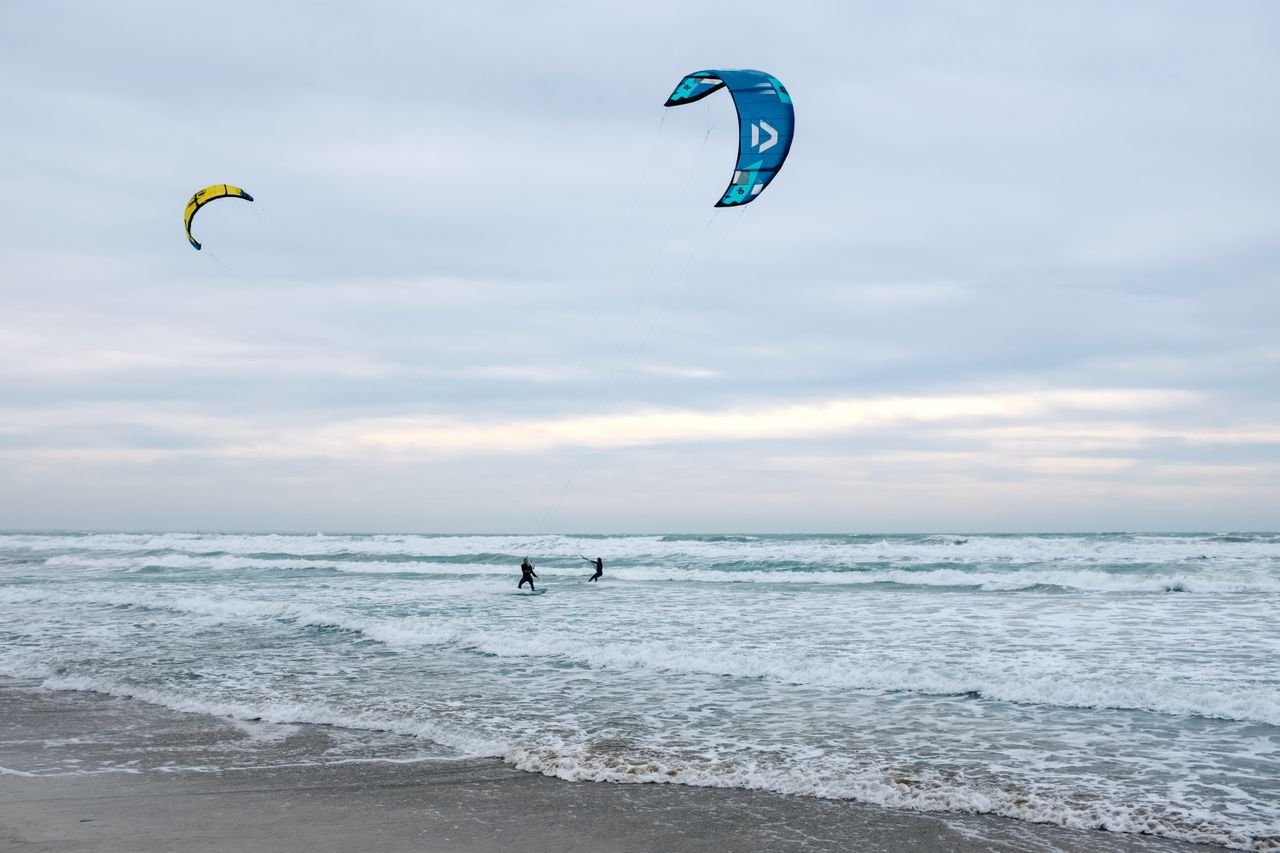 Two kitesurfers enjoying the waves under a cloudy sky on a brisk coastline.