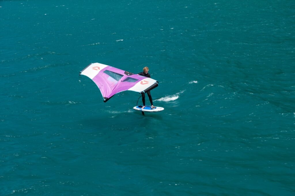 A person wing foiling across a vibrant turquoise lake, showcasing thrilling water sport action.