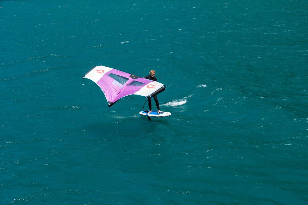 A person wing foiling across a vibrant turquoise lake, showcasing thrilling water sport action.